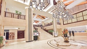 Um hall amplo com escadaria central, balcão de recepção e uma fonte decorativa.