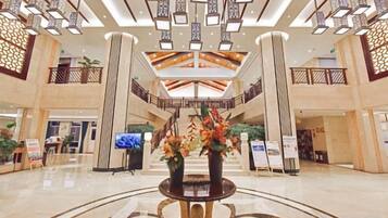 A spacious lobby with a central reception desk, high ceilings with modern lighting fixtures, and a view of the upper level.
