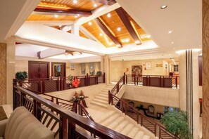 A hotel lobby with a central staircase, multiple seating areas, and a high ceiling with exposed beams. - Yuntian Garden Hotel (Kunming)