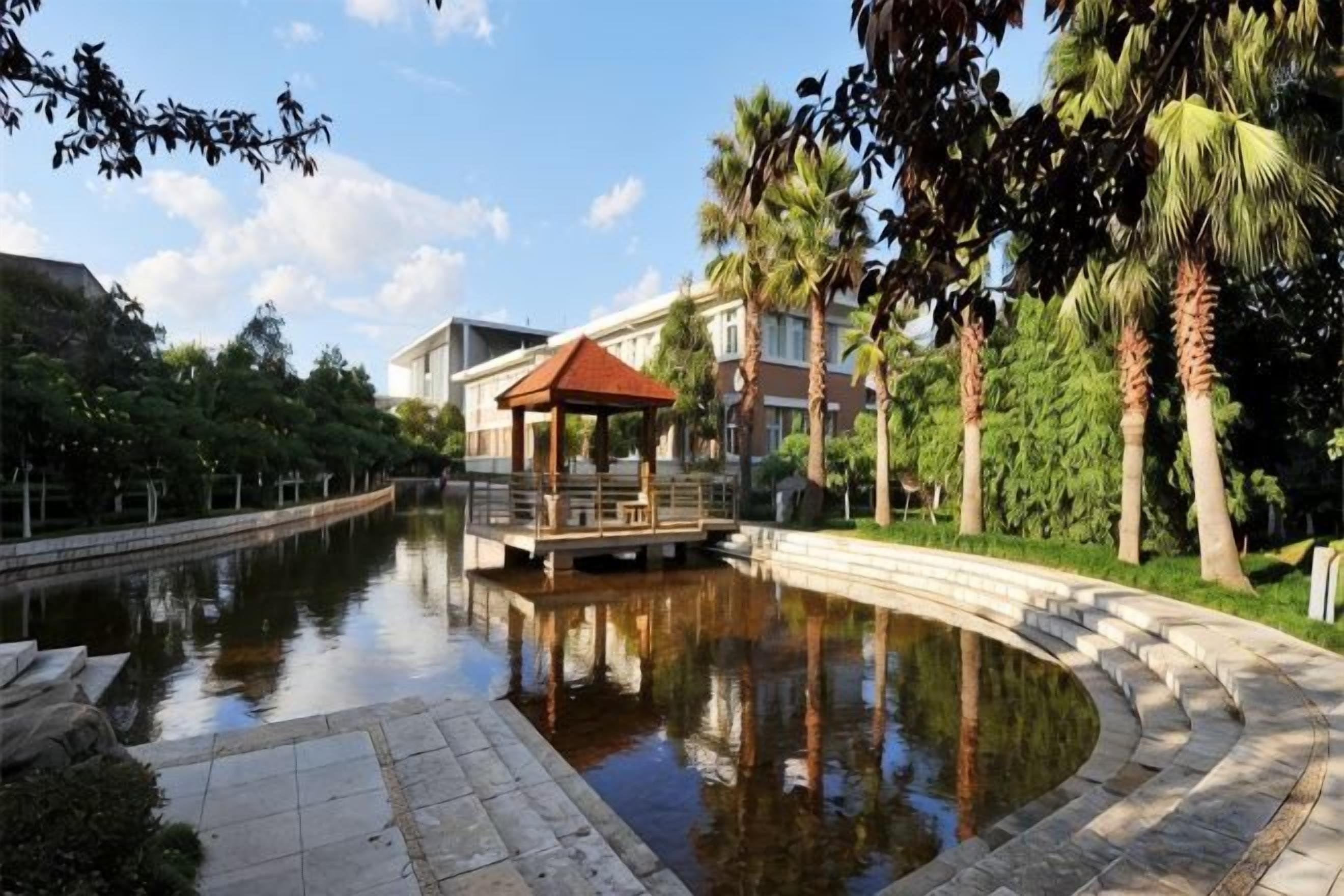 A tranquil water body with a gazebo, a pathway, and a building with a red roof.