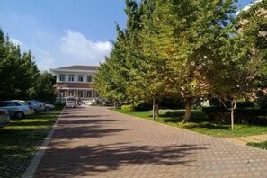 A paved pathway lined with trees and parked cars, leading to a building with a red roof. - Yuntian Garden Hotel (Kunming)
