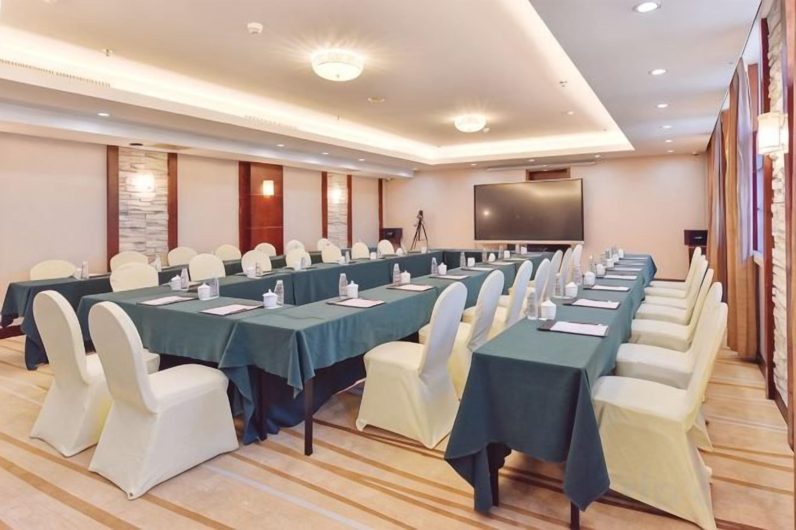 A conference room with long tables, chairs, and a large screen.