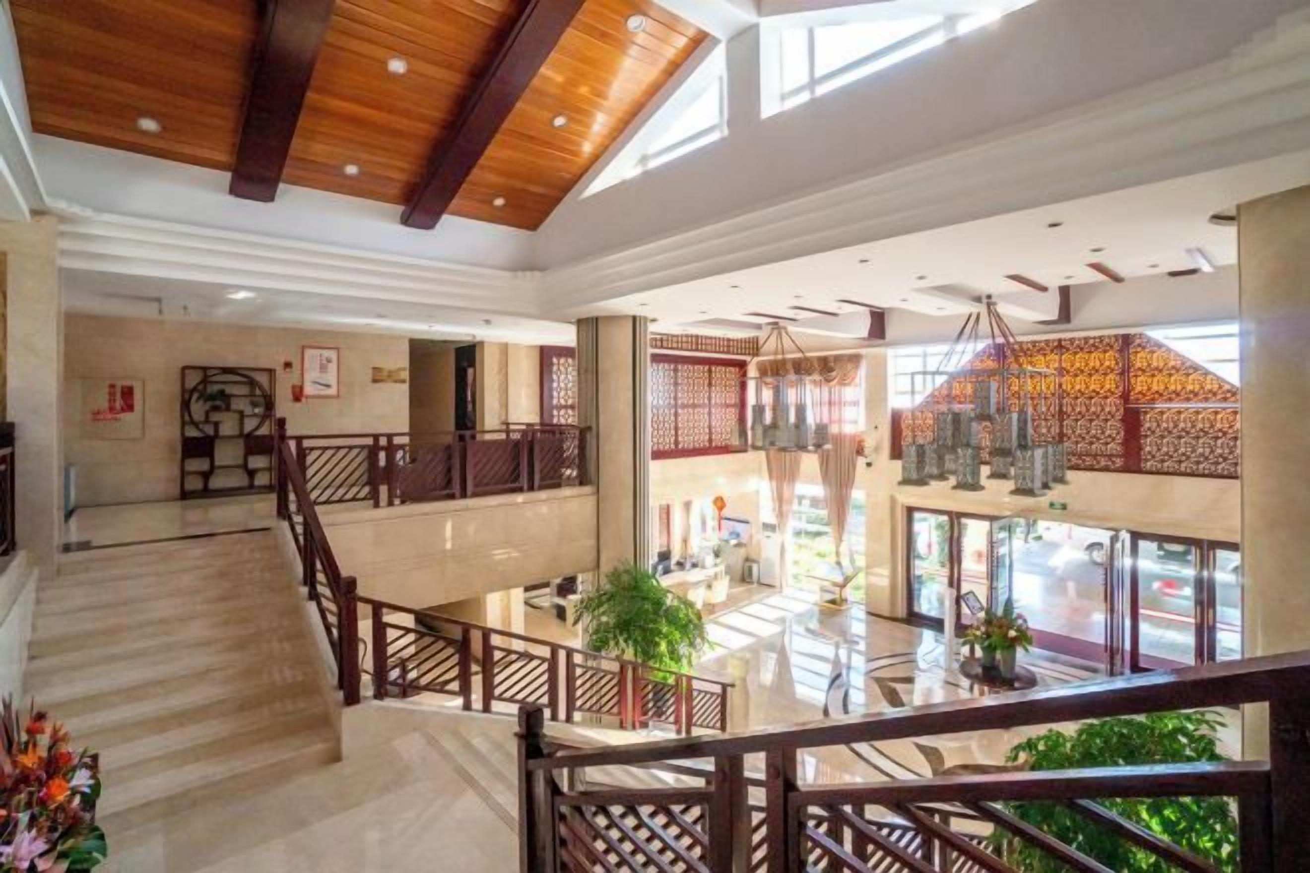 A spacious hotel lobby with a central staircase, a reception desk, and a view of the street through large windows.