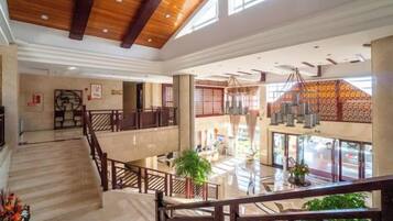 A spacious hotel lobby with a central staircase, a reception desk, and a view of the street through large windows.