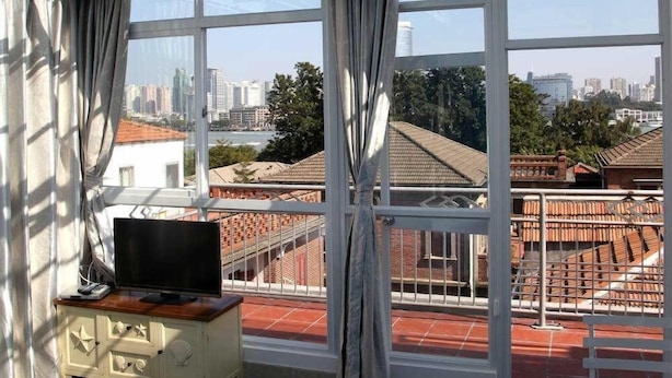 Ein Zimmer mit einem Bett, einem Fernseher auf einer Kommode und Blick auf eine Stadtlandschaft durch große Fenster.