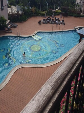 A swimming pool with a person swimming, surrounded by lounge chairs and umbrellas.