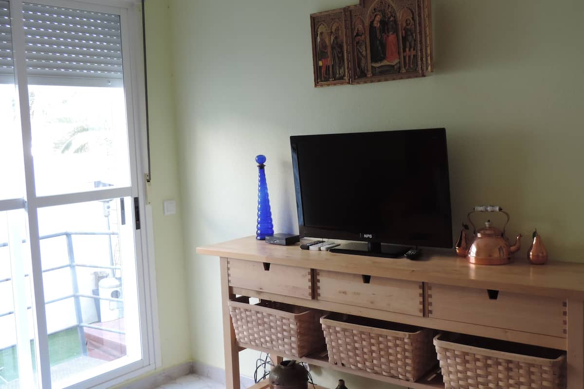 Ein Zimmer mit Fernseher auf einem Holzständer, einer blauen Vase und einem Gemälde darüber.