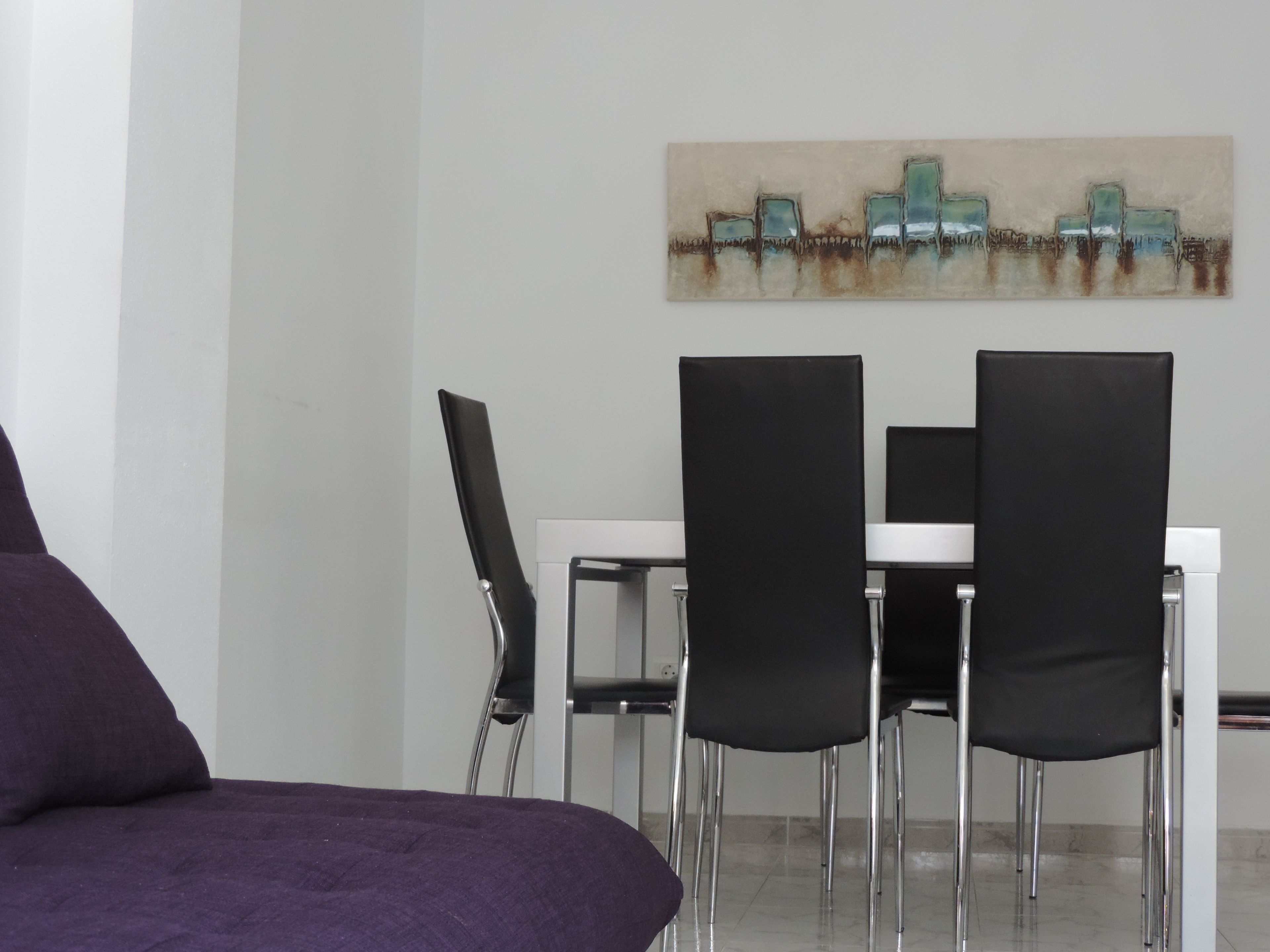 Ein Essbereich mit einem weißen Tisch und vier schwarzen Stühlen. Eine violette Couch befindet sich im Vordergrund.