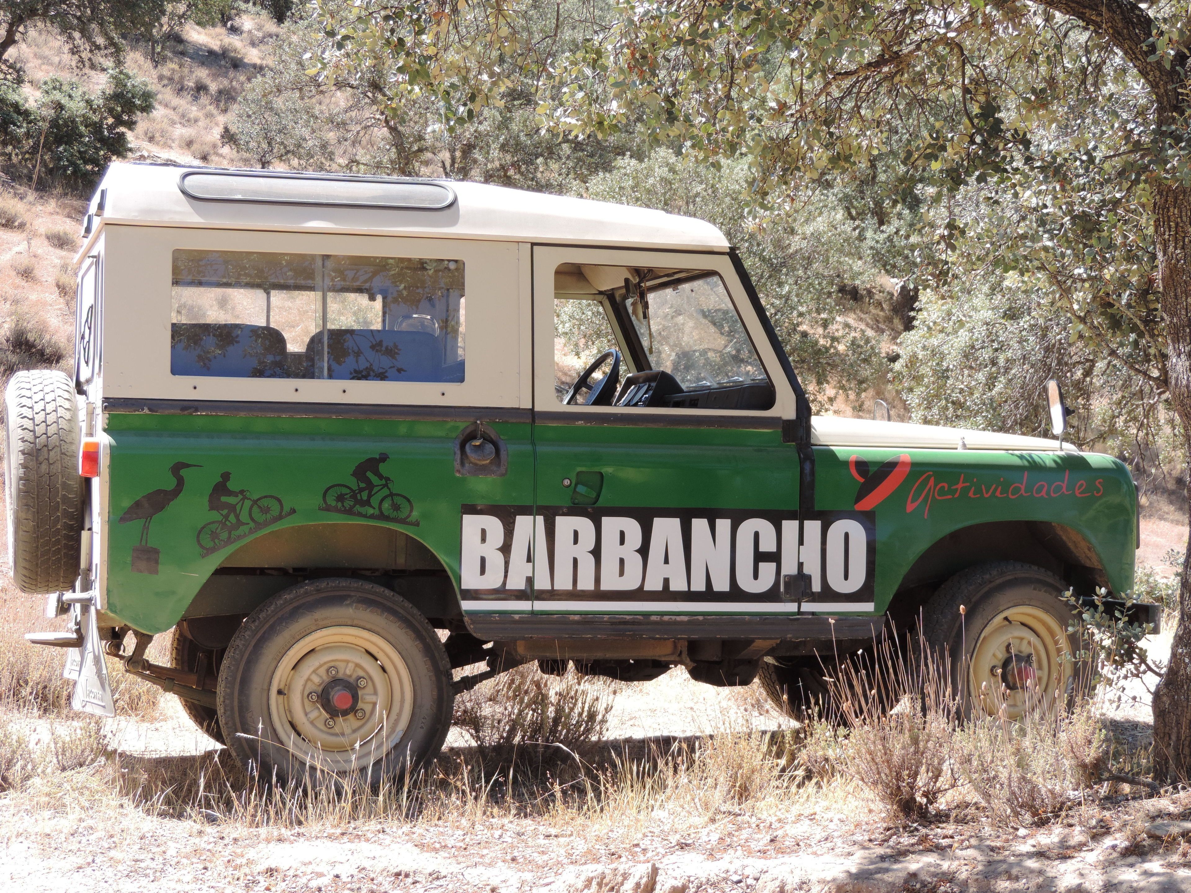 A green and beige vehicle with "BARBANCHO" and "Actividades" written on it, parked in a natural setting.