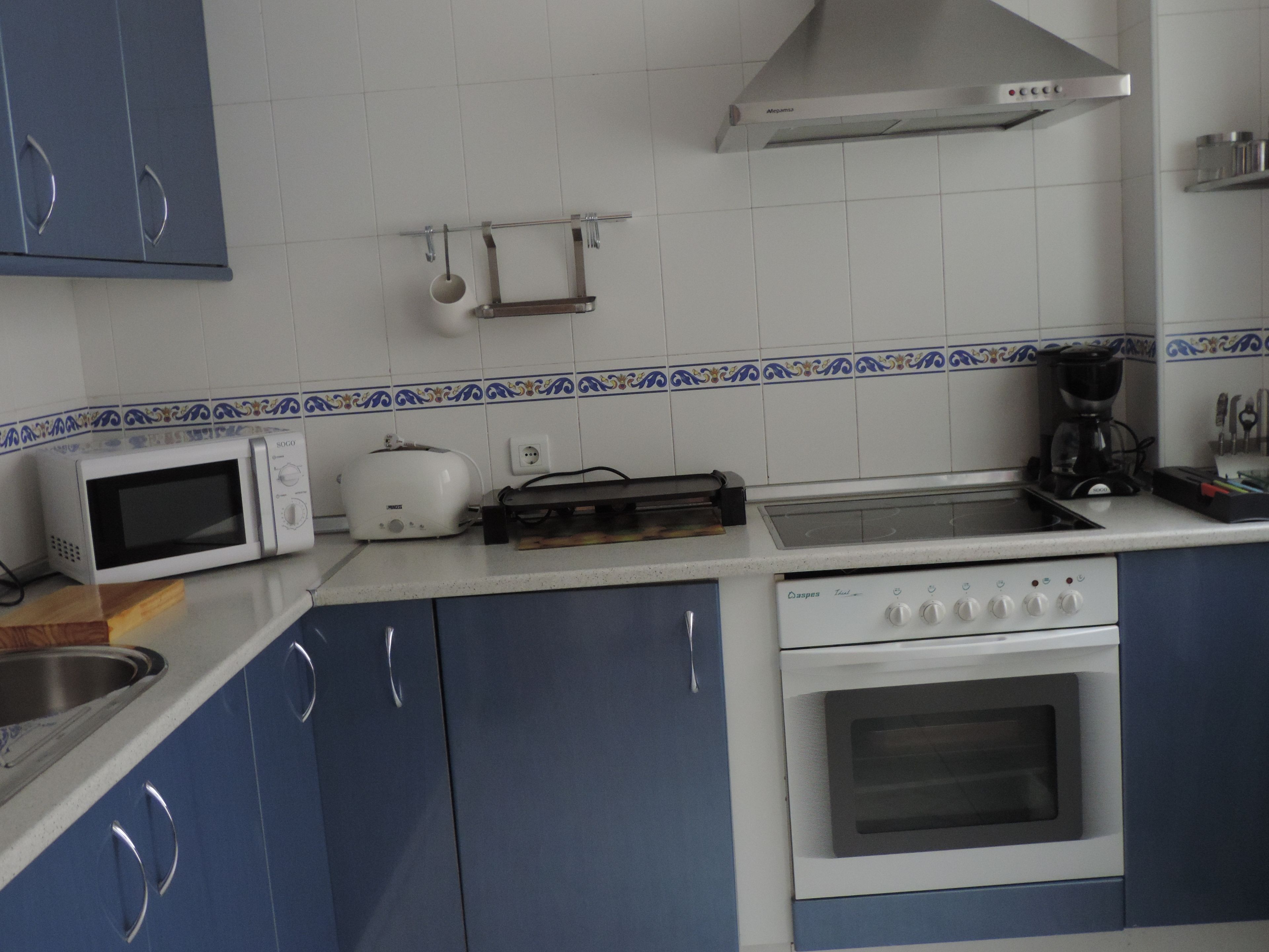 A kitchen with blue cabinets, a white microwave, a toaster, a coffee maker, and a stove.