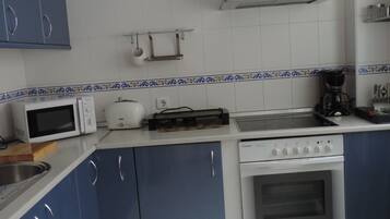 A kitchen with blue cabinets, a white microwave, a toaster, a coffee maker, and a stove.
