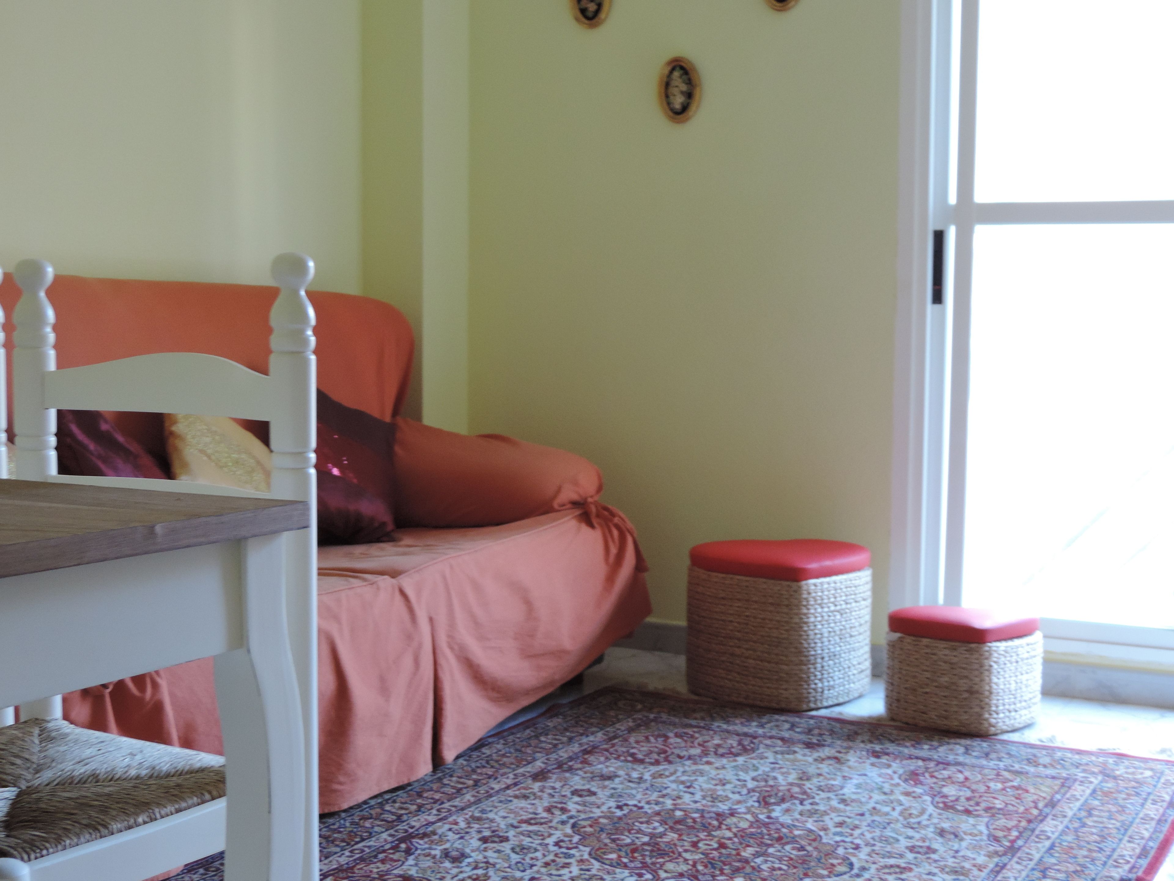 Una habitación con una cama, una silla, una mesa y dos otomanas.