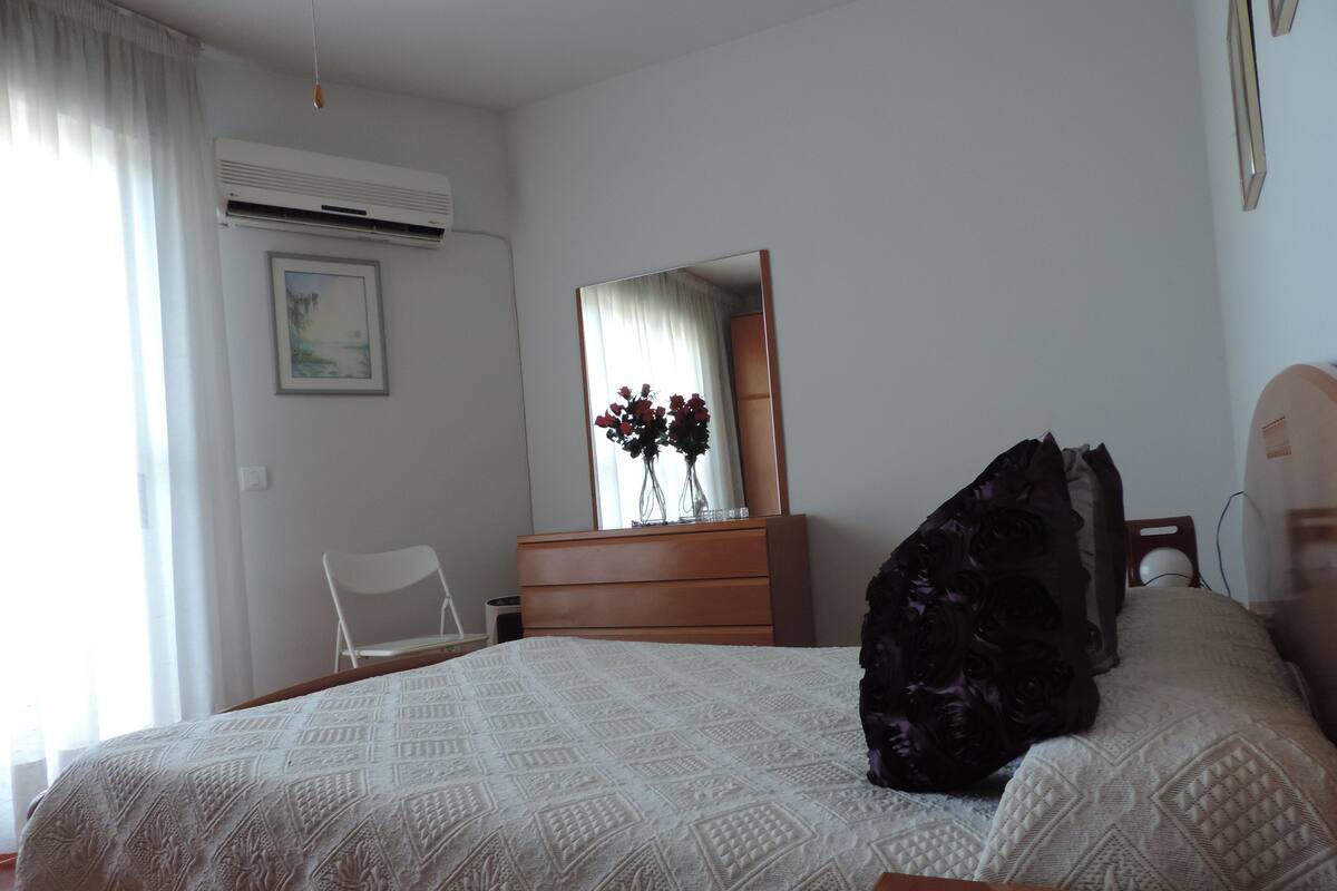 Ein Schlafzimmer mit Bett, Kommode, Stuhl und Spiegel.