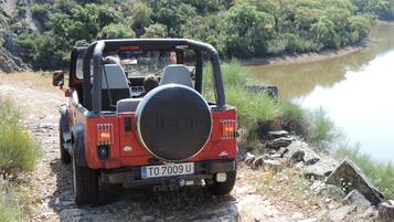 A red Jeep with a spare tire mounted on the back, parked on a rocky path beside a river.