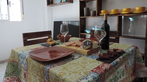 A dining table with a patterned tablecloth, a bottle of wine, a cheese board, and a bowl of bread. - Apartamentos Barbancho (Casar de Caceres)