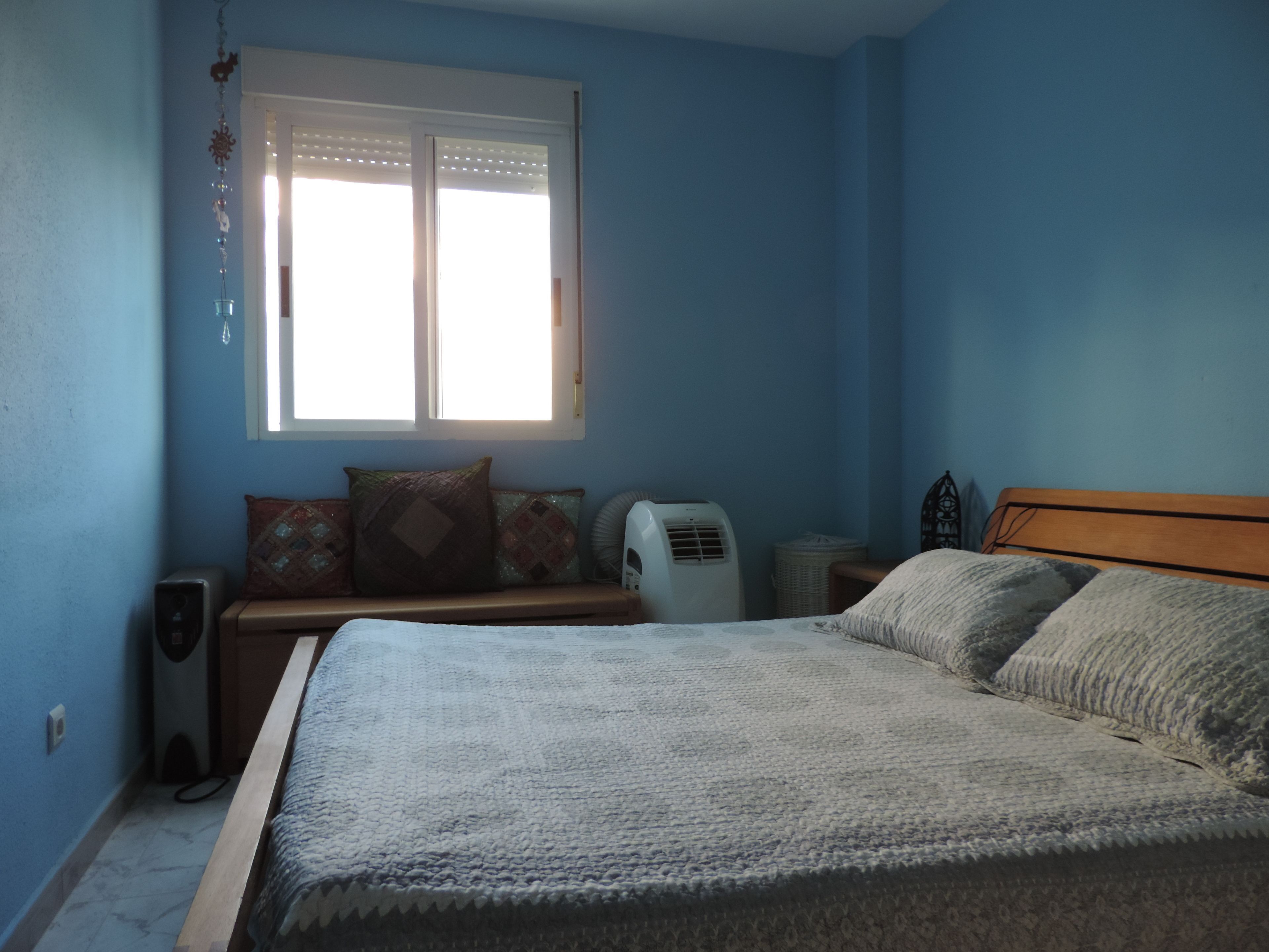 Een slaapkamer met een bed, een raam, een heater en een speakersysteem aan de muur.
