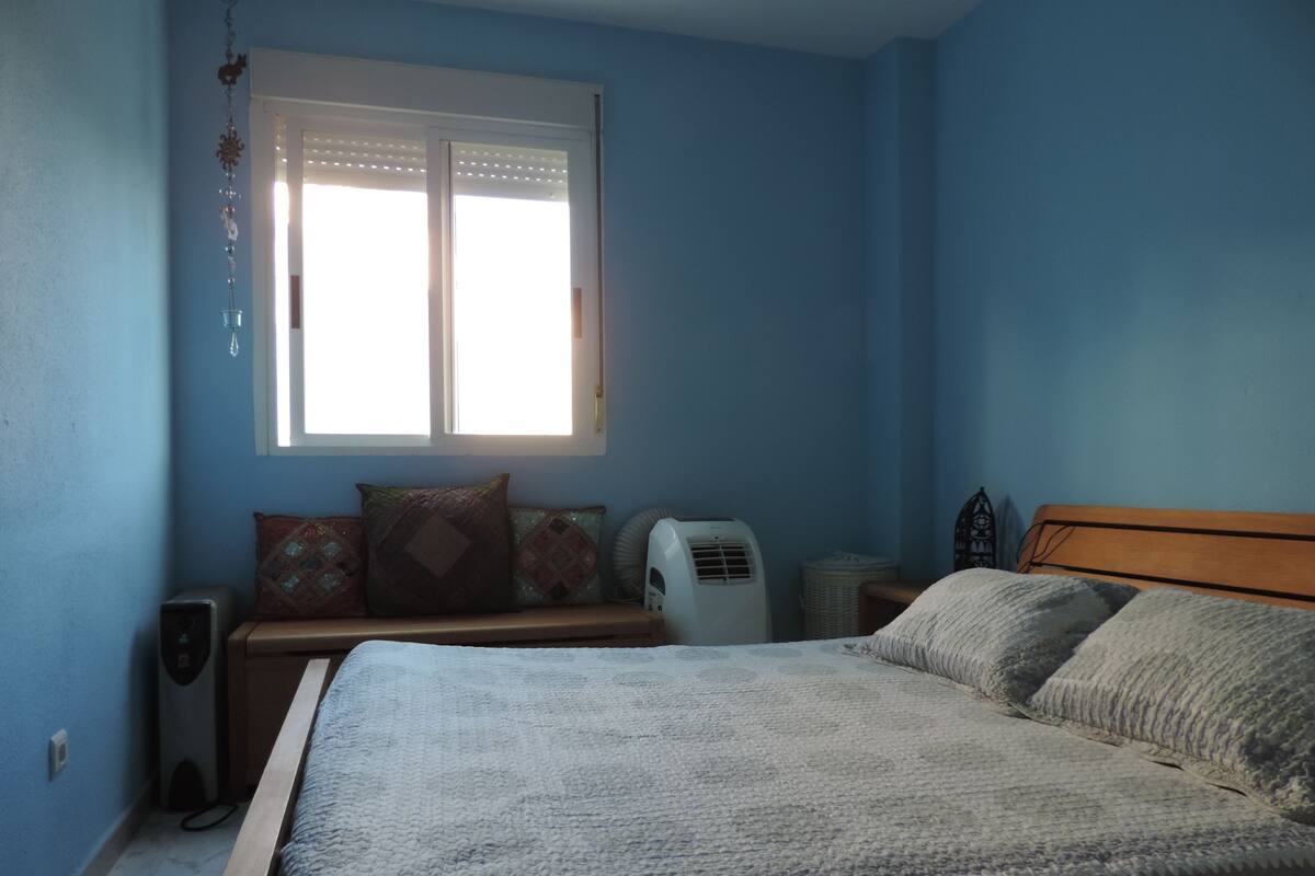 Een slaapkamer met een bed, een raam, een heater en een speakersysteem aan de muur.