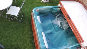 A hot tub with a control panel, surrounded by artificial grass, a table, and chairs. - Apartamentos Barbancho (Casar de Caceres)