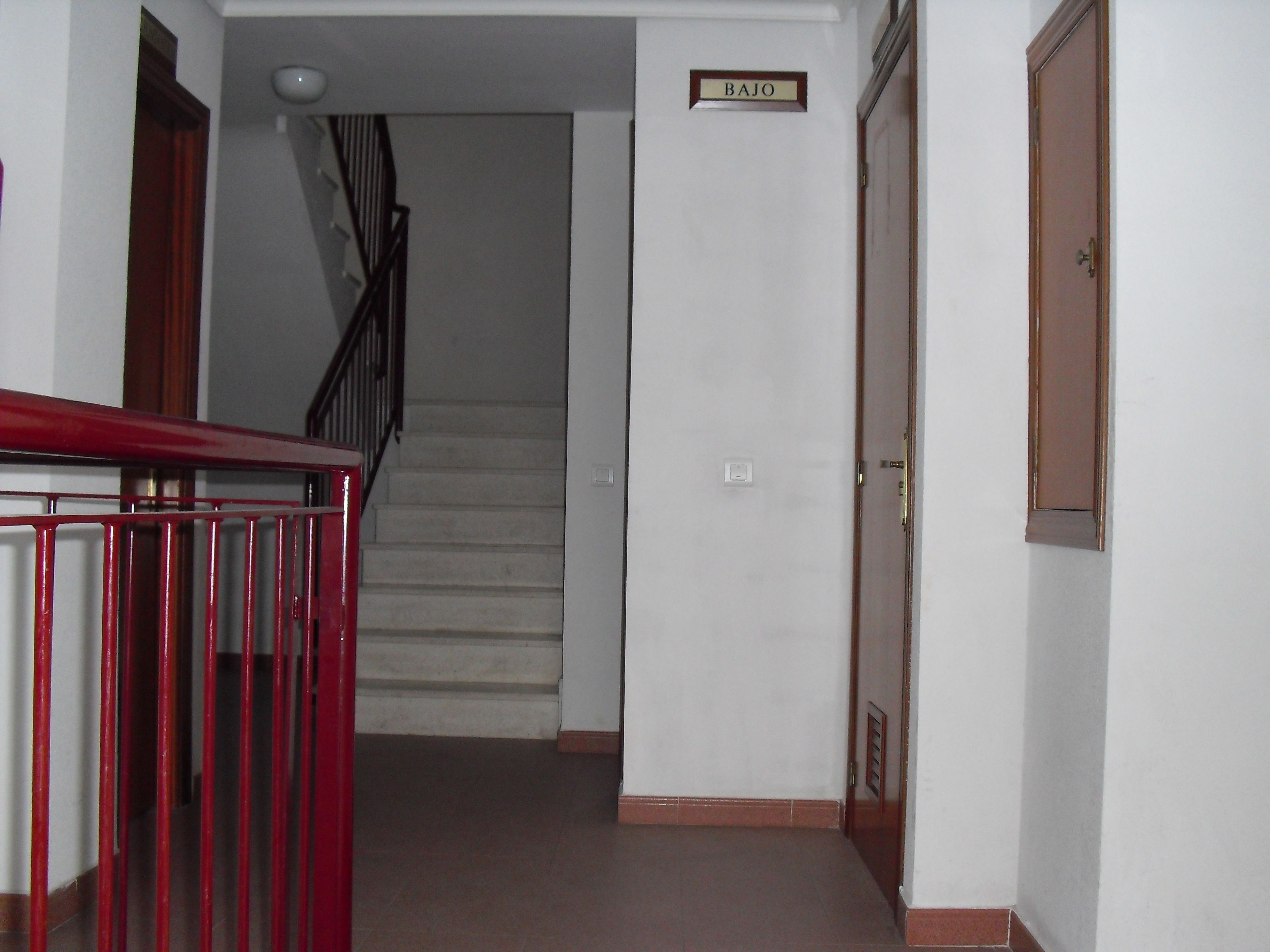 Un escalier menant à une pièce portant l’inscription « BAJO », avec une rampe rouge et une porte en bois.