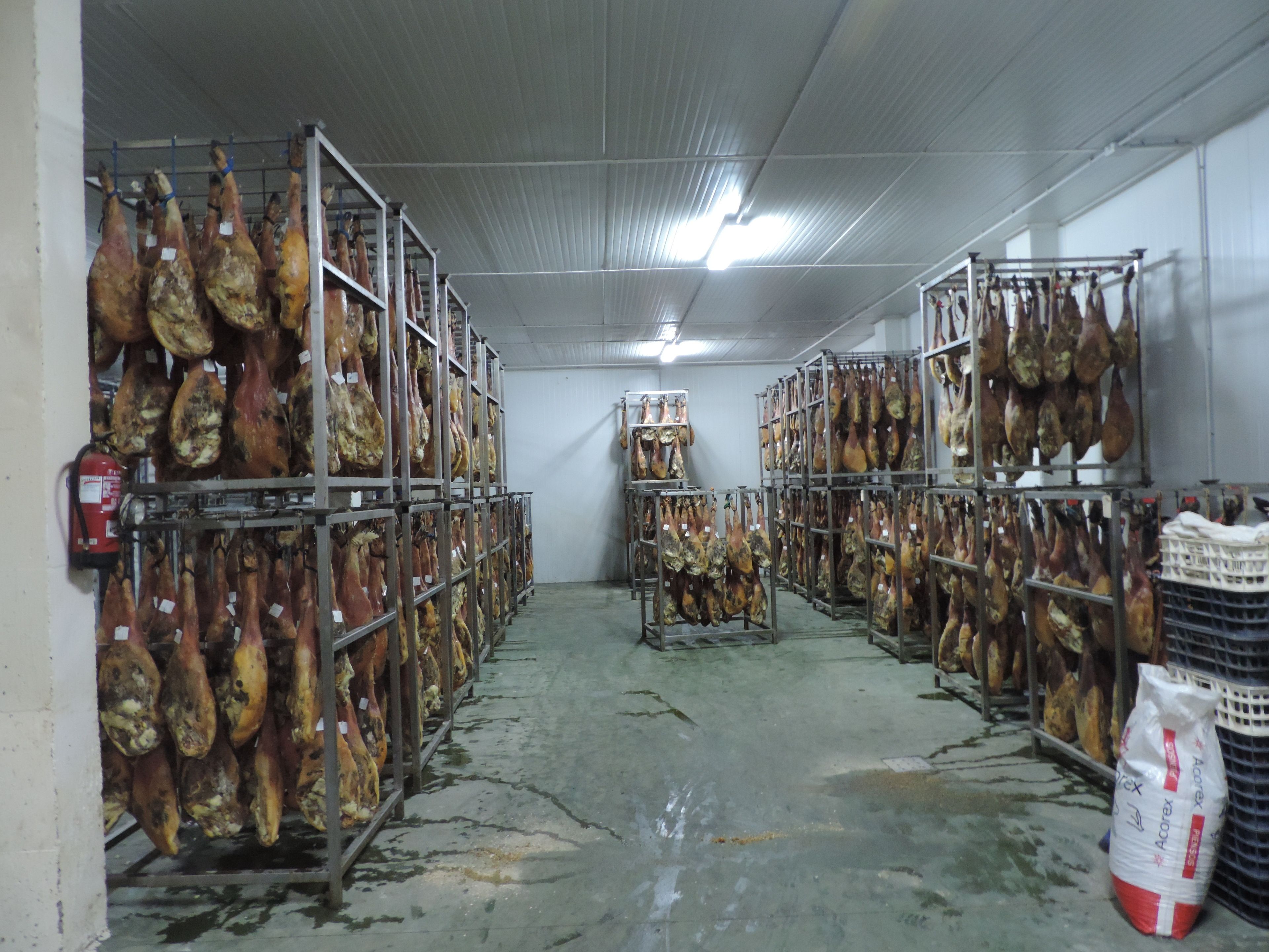 Un almacén con hileras de productos cárnicos colgados en estanterías metálicas.