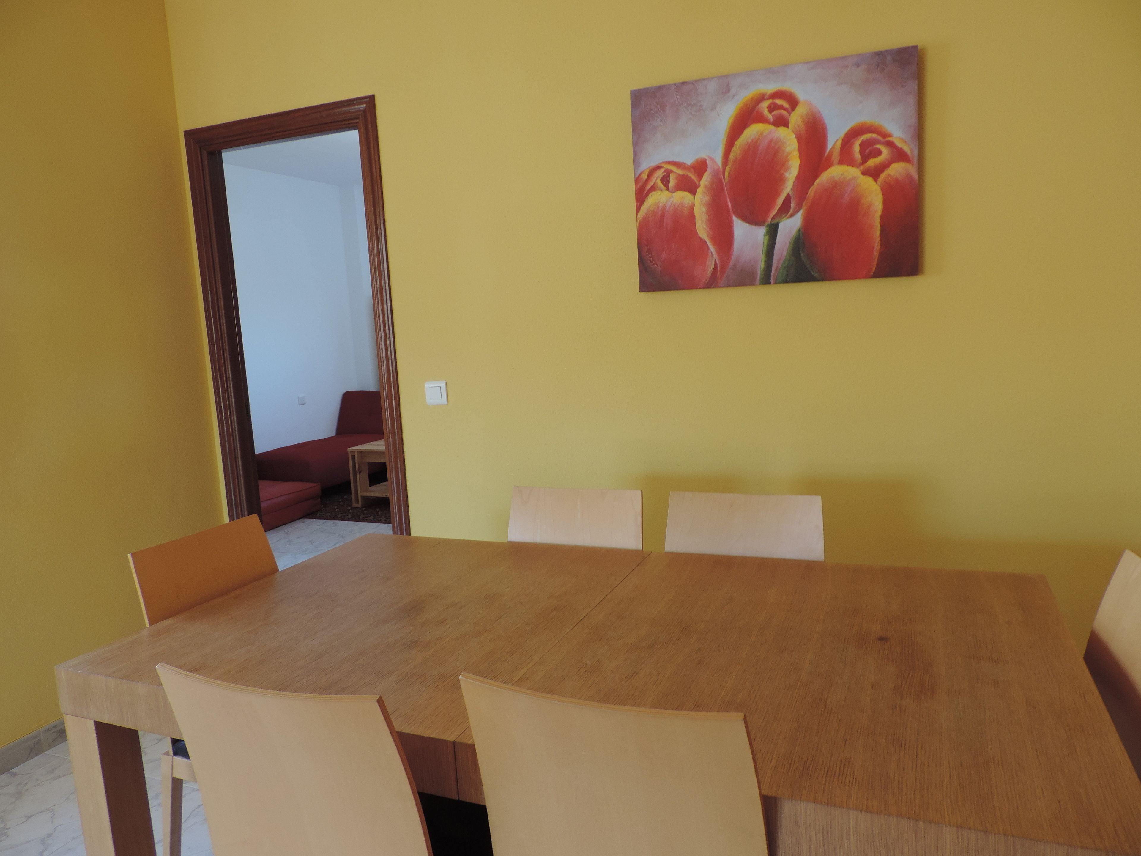 Ein Essbereich mit einem Holztisch und beigen Stühlen, einem Gemälde mit Tulpen an der Wand und einer Tür zu einem anderen Raum.