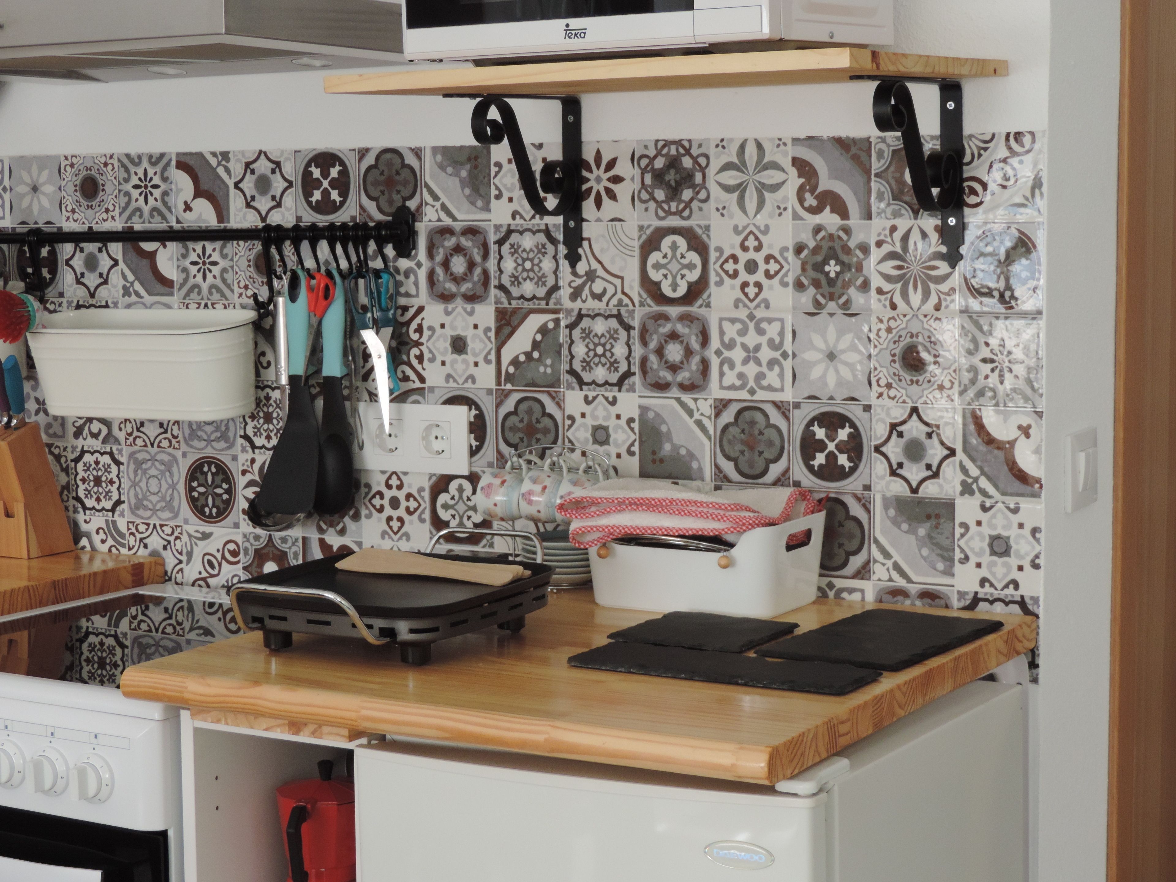 A kitchen with a microwave, a stove, and a wooden countertop. There are various kitchen utensils hanging on hooks, and a white appliance with a logo.