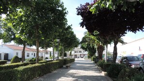 A paved pathway lined with neatly trimmed hedges and trees, leading to a building with a tiled roof. - Apartamentos Barbancho (Casar de Caceres)