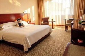 A hotel room with a large bed, a wooden headboard, a small round table with a lamp, a chair, and a desk with a plant. - New Era Hotel (Shanxi Provincial Government) (Taiyuan)