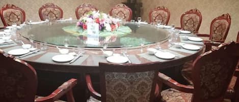 A round table with a glass top surrounded by ornate chairs, set for a meal.