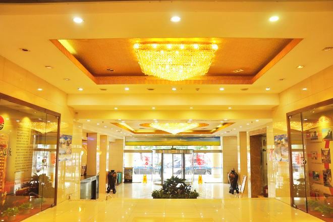 A hotel lobby with a chandelier, a reception desk, and a glass storefront.