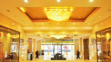 A hotel lobby with a chandelier, a reception desk, and a glass storefront.