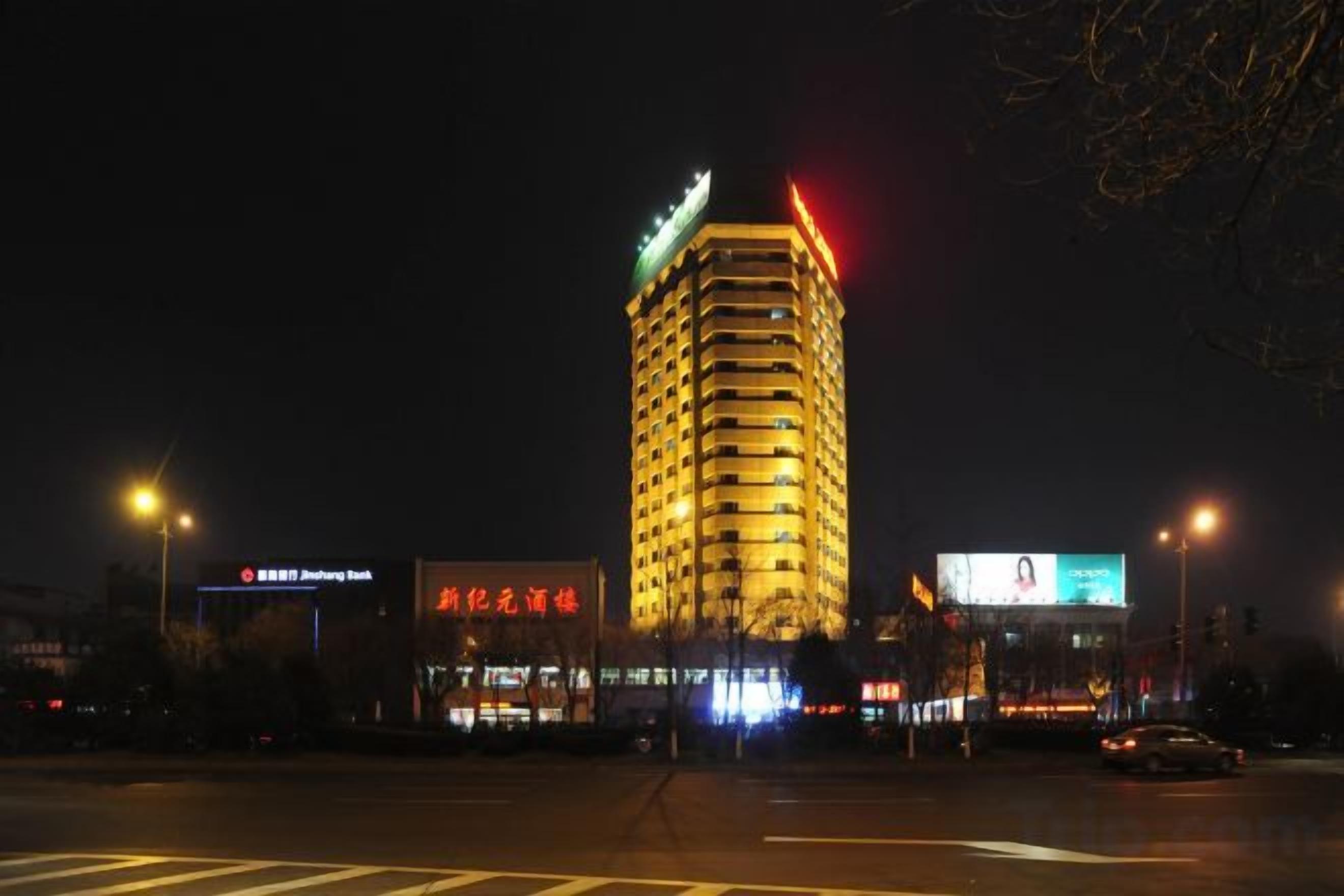 Un immeuble à plusieurs étages, doté d’une enseigne lumineuse, d’une entrée imposante et d’un passage piéton au premier plan.
