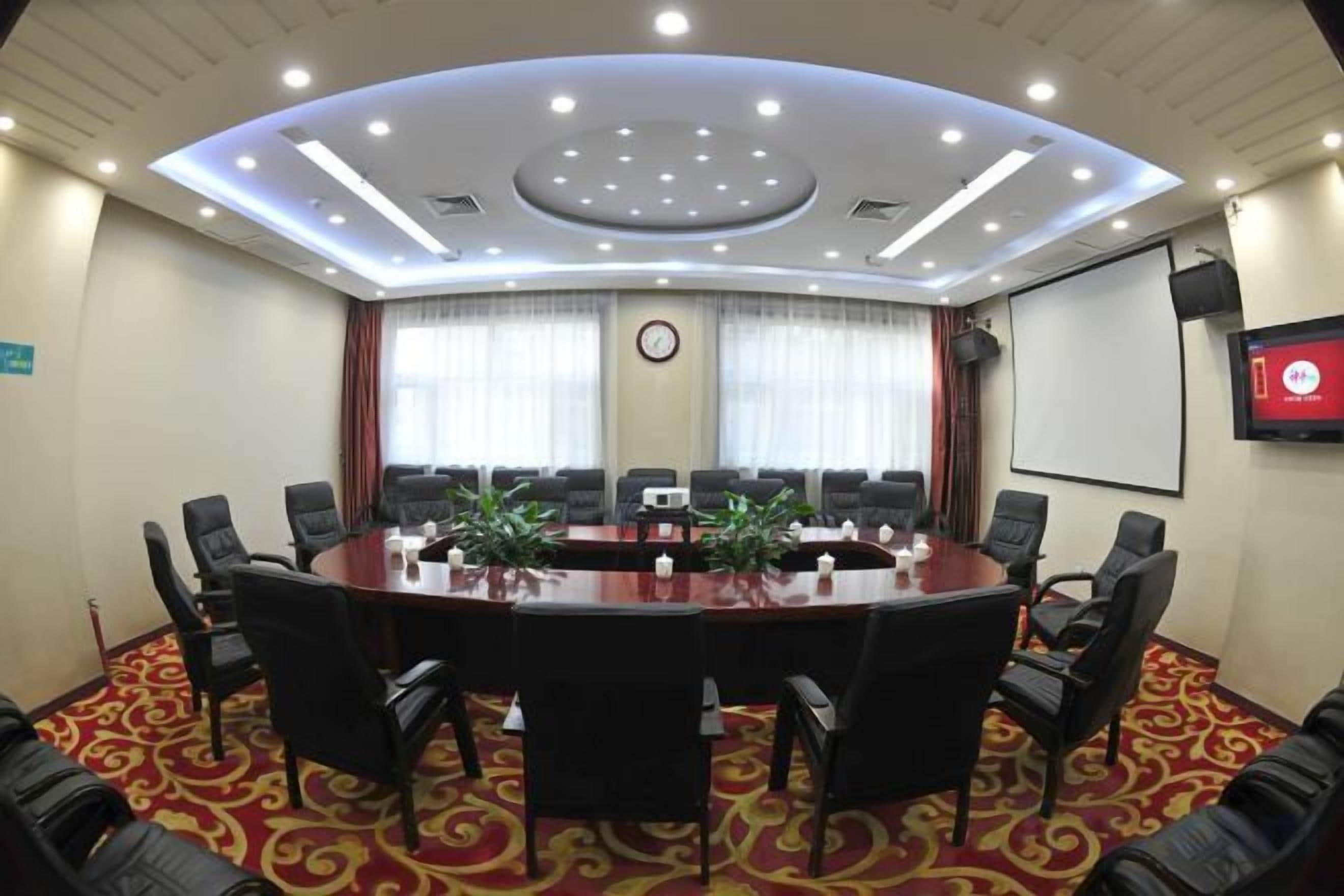 A conference room with a large oval table, multiple chairs, a projector screen, and a clock on the wall.