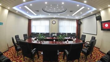 A conference room with a large oval table, multiple chairs, a projector screen, and a clock on the wall.