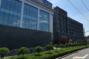 A modern building with a glass facade, a flat roof, and a series of trees along the sidewalk. - New Era Hotel (Shanxi Provincial Government) (Taiyuan)