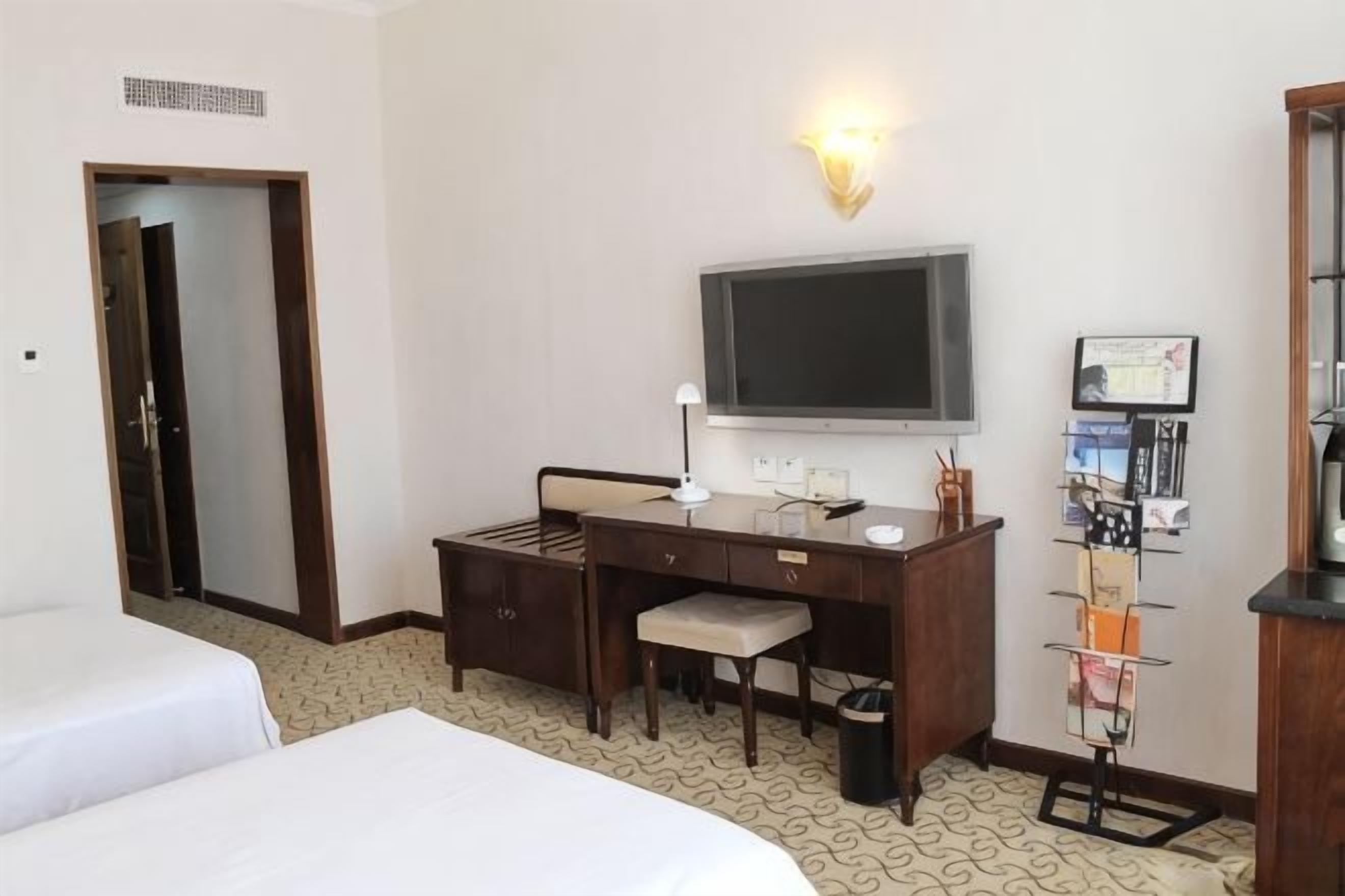 Ein Hotelzimmer mit Bett, Schreibtisch, Stuhl, Fernseher und einem Wandfernseher.
