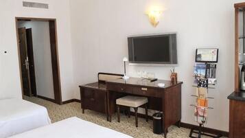 Ein Hotelzimmer mit Bett, Schreibtisch, Stuhl, Fernseher und einem Wandfernseher.