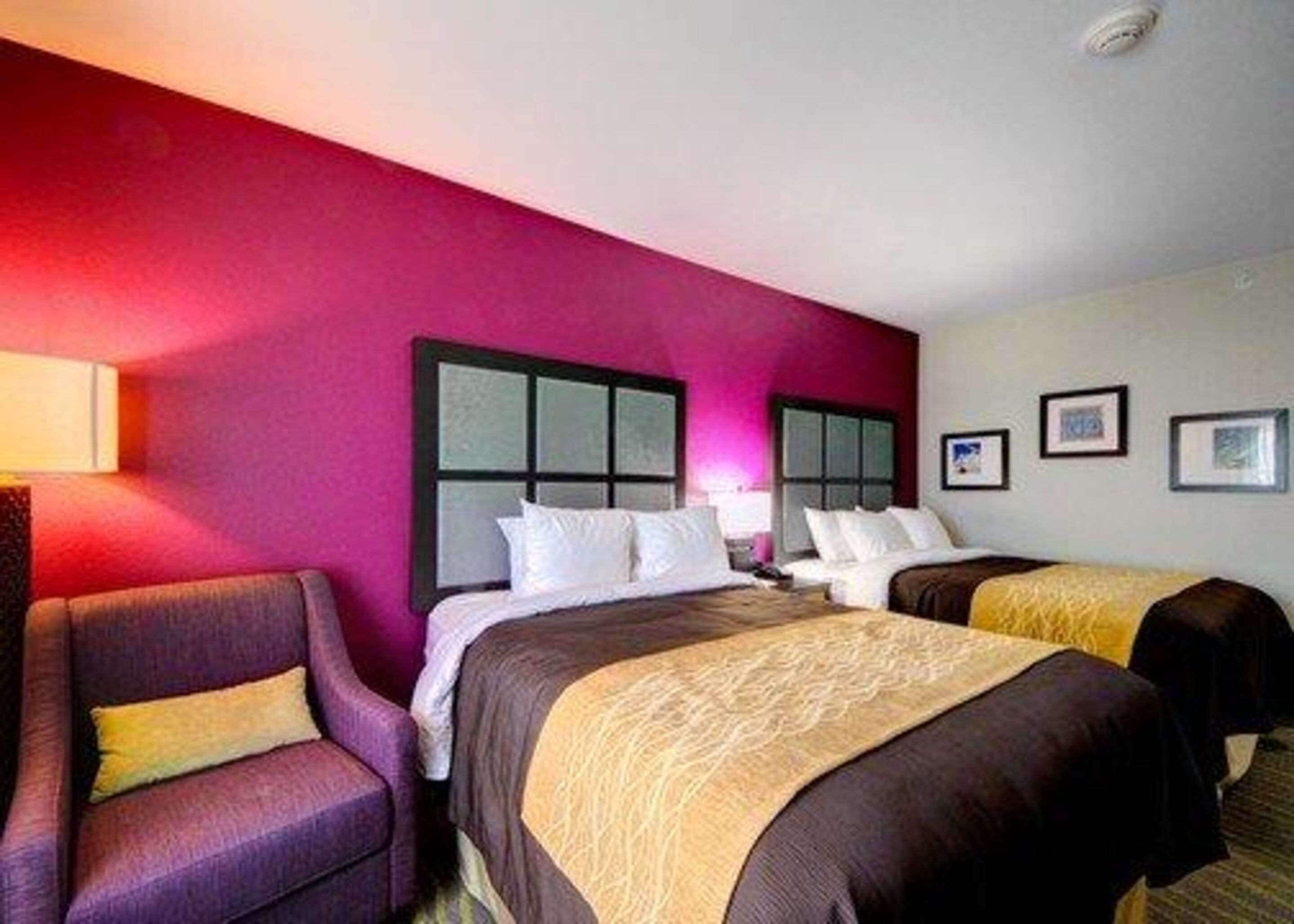 A hotel room with two beds, a purple armchair, and a wall with framed pictures.
