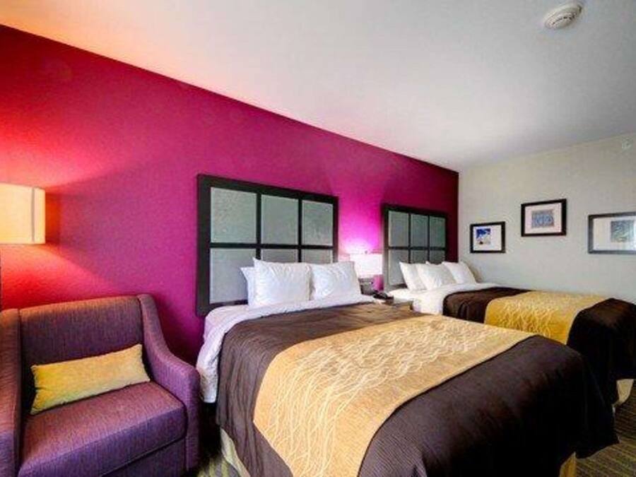 A hotel room with two beds, a purple armchair, and a wall with framed pictures.