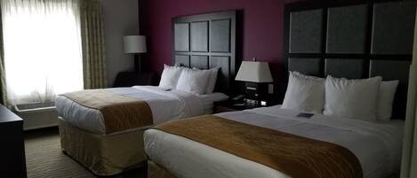 A hotel room with two beds, a desk, a lamp, and a window with curtains.