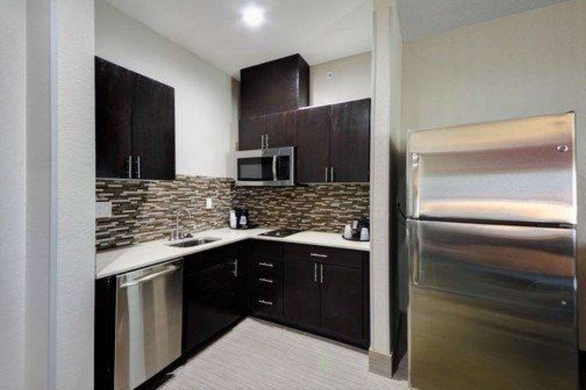 A modern kitchen with dark cabinets, a stainless steel refrigerator, a microwave, and a dishwasher.