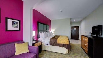 Una habitación de hotel con una cama, un sofá morado, un aparador y un televisor.