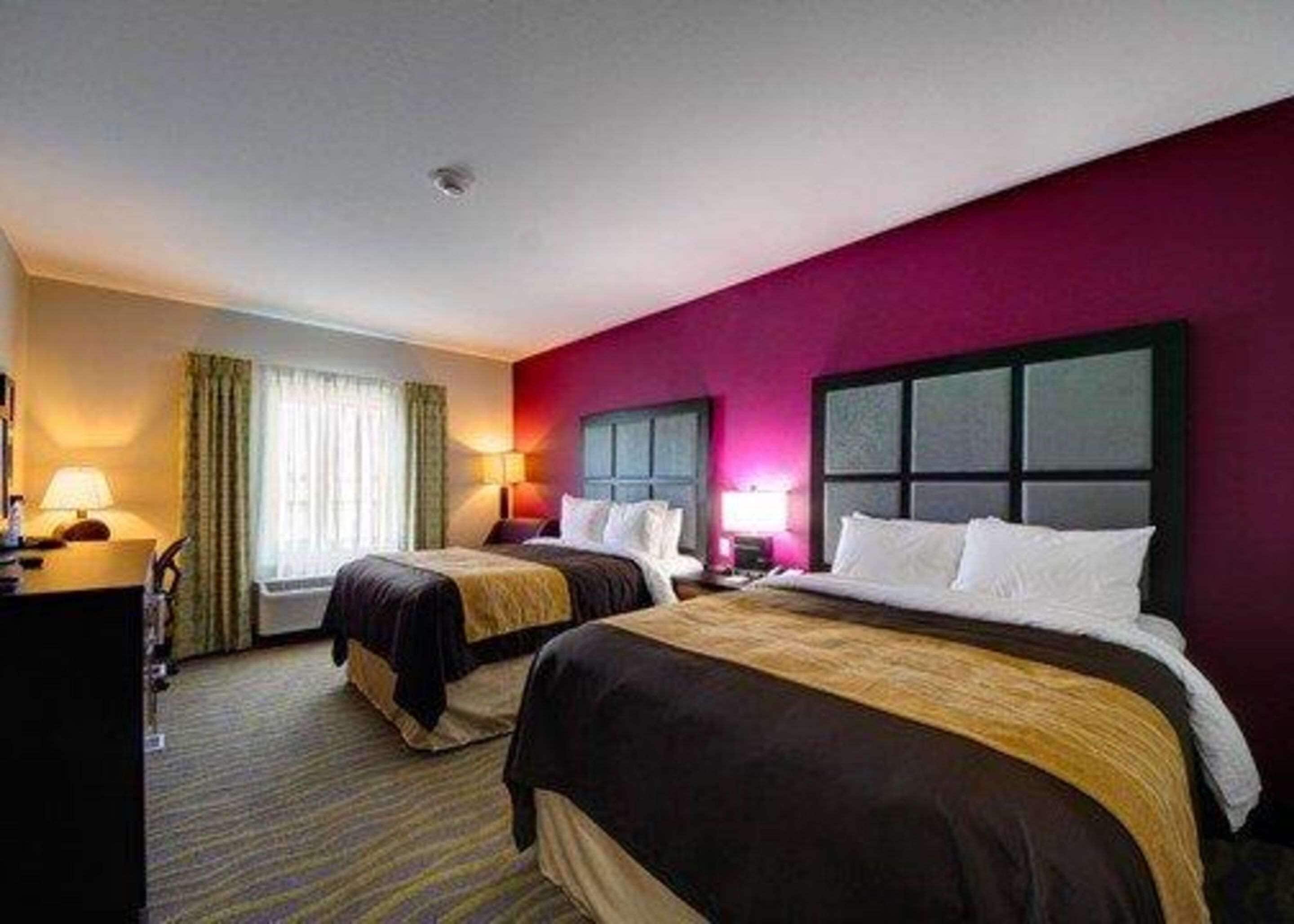 Habitación de hotel con dos camas, un escritorio y ventana con cortinas.