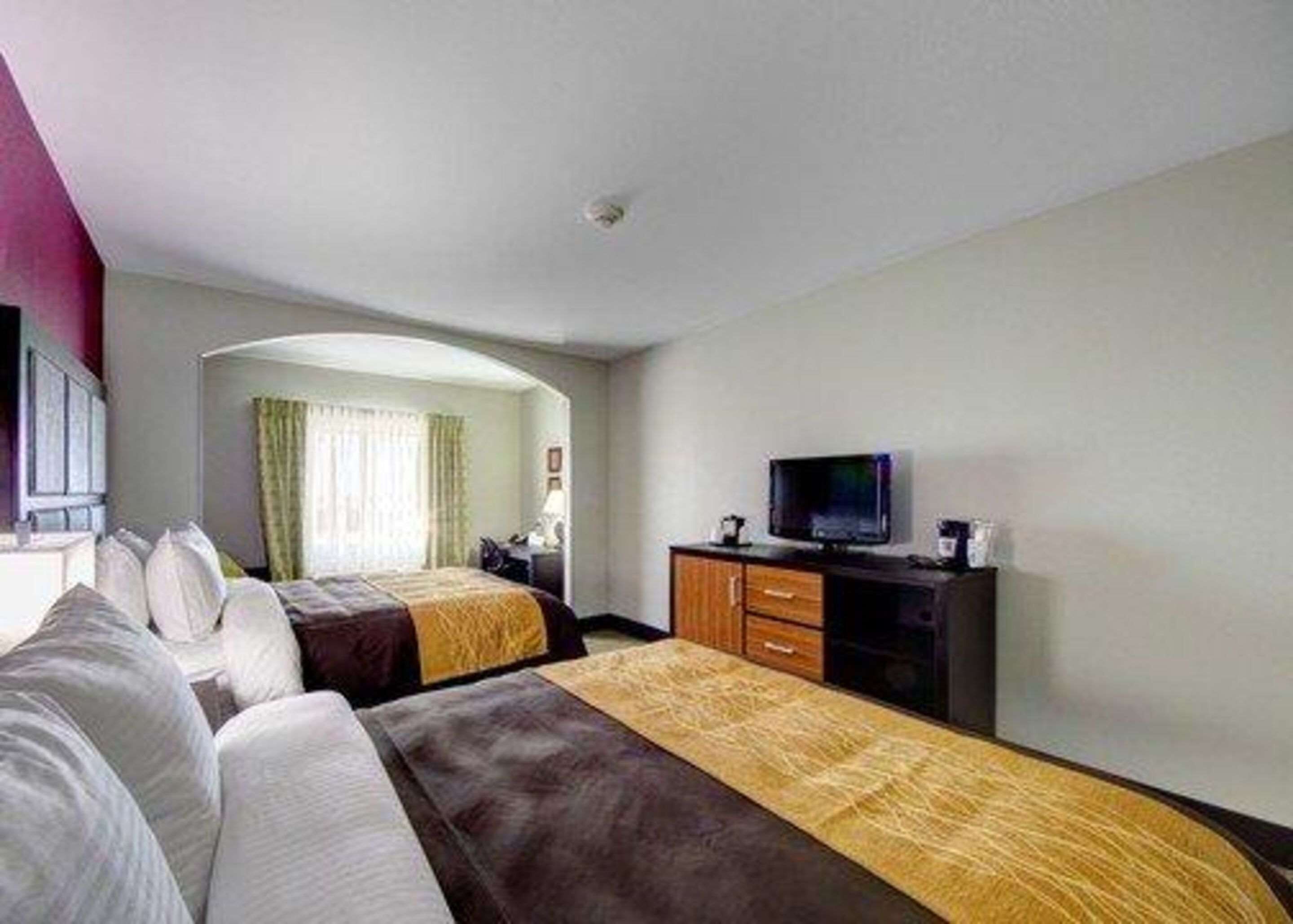 A hotel room with two beds, a television, and a desk with drawers.