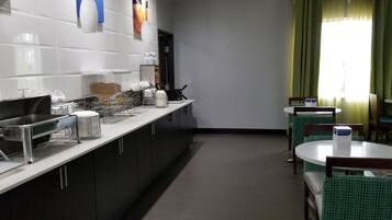 Een schone, moderne keuken met roestvrijstalen apparatuur, een buffetopstelling en een zithoek met groene stoelen en een ronde tafel.