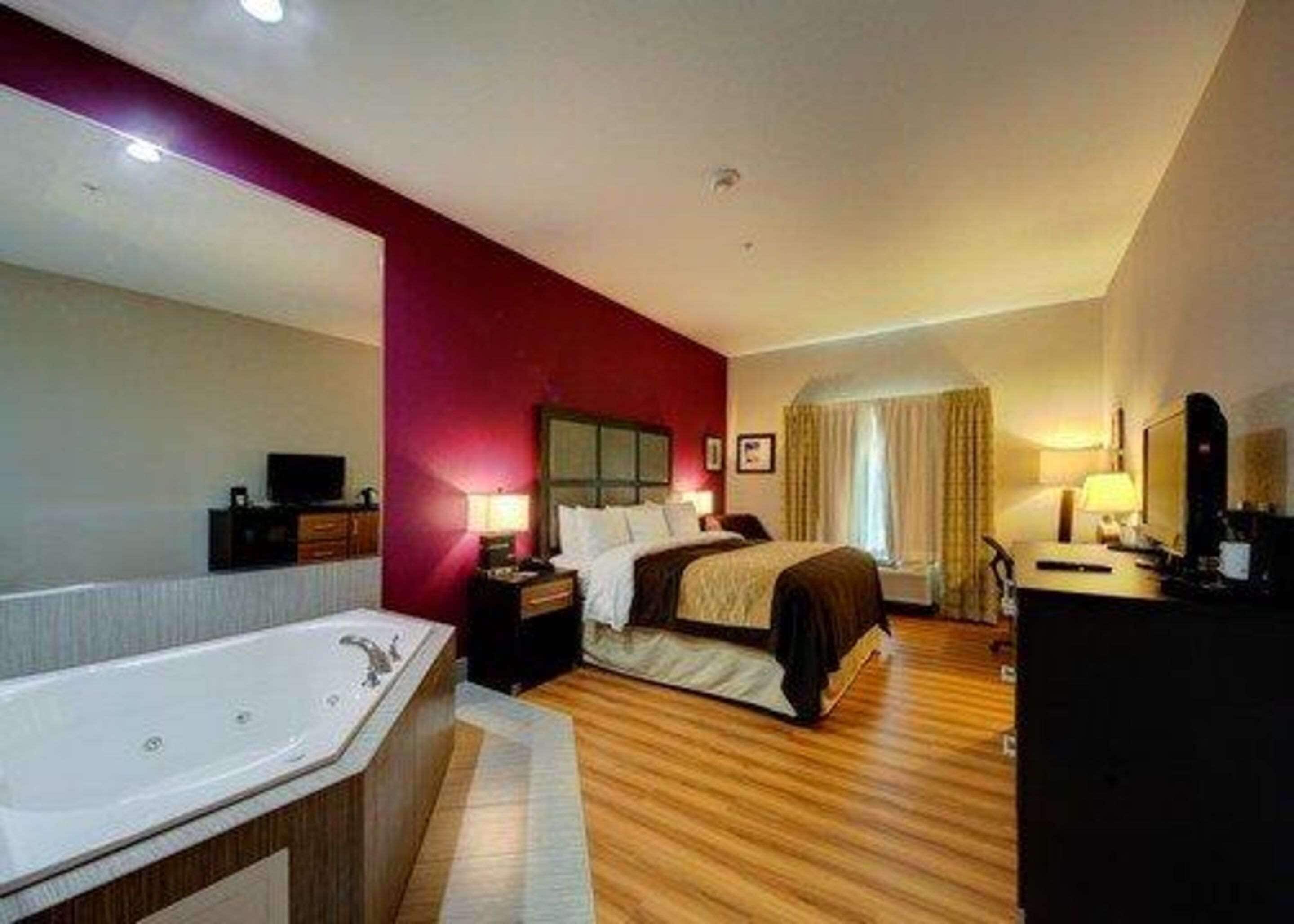 A hotel room with a large bed, a separate bathroom with a bathtub, a desk with a computer, and a TV.