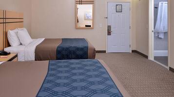 Hotelkamer met een bed, een bureau met telefoon, een spiegel, een deur en een zichtbare badkamer door een geopende deur.