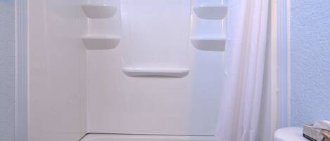 A white bathtub with a shower curtain, a towel, and a small shelf.