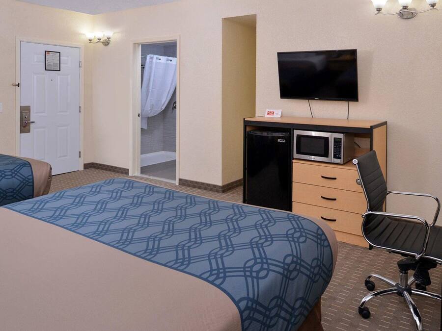 Habitación de hotel con dos camas, un escritorio con microondas, televisor y zona de ducha.