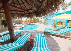 A pool area with lounge chairs and umbrellas. - Aruba Palms Escape Suites (Noord)